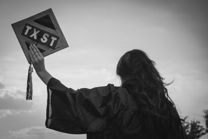 Graduate raising a TX-ST sign, black and white