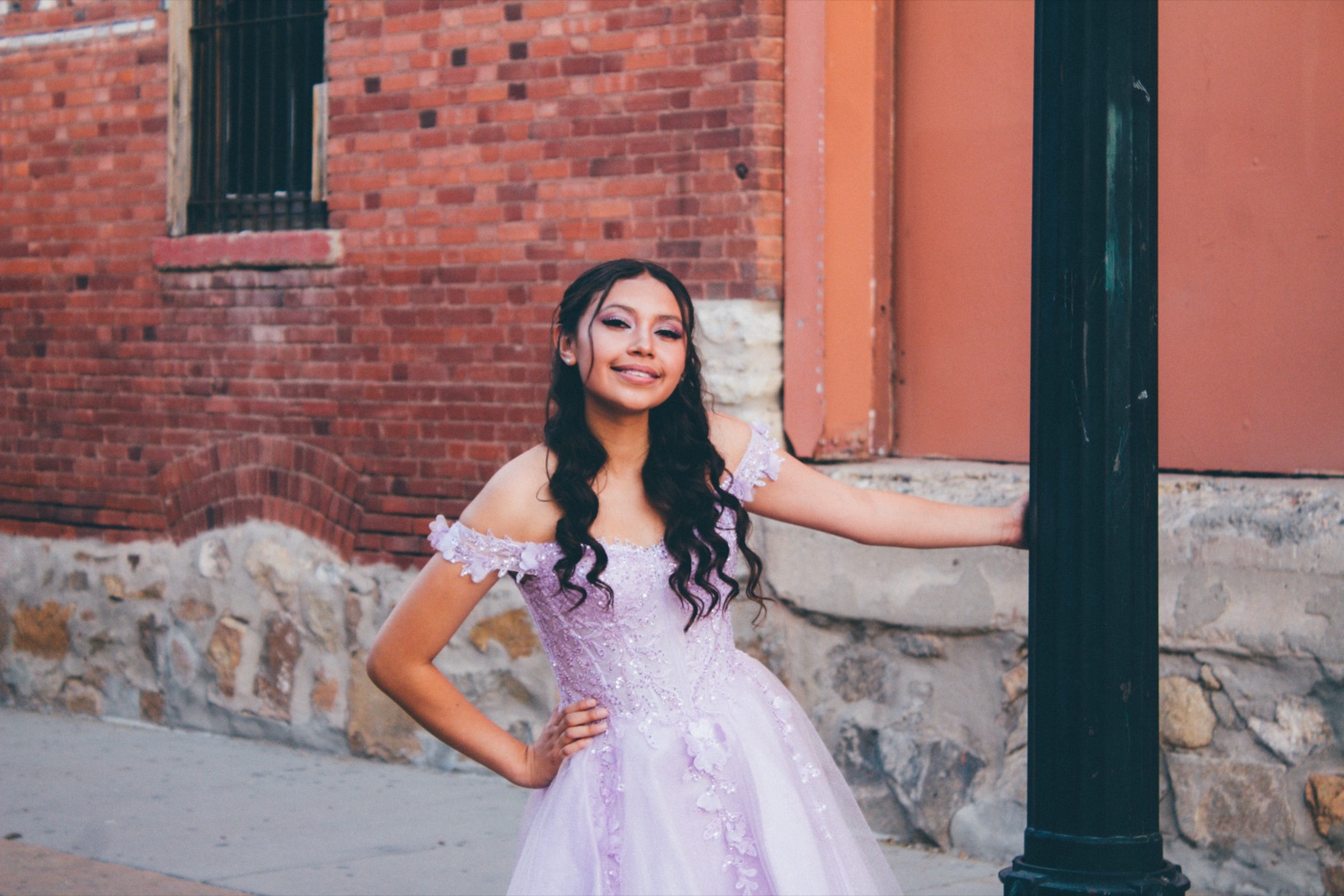 Quinceañera in a pink gown against a brick wall